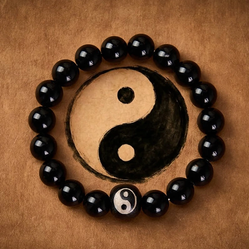 Black obsidian yin yang beaded bracelet with engraved centerpiece on brown leather background top view