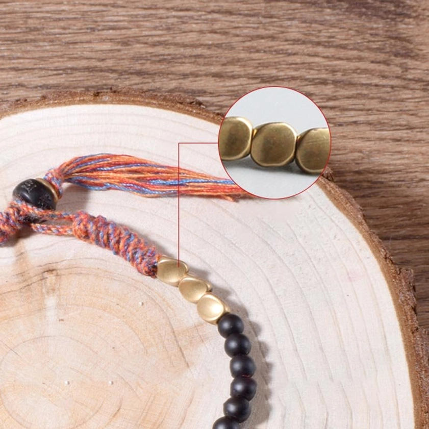 Close-up detail shot of black onyx bracelet clasp, gold spacer beads, and woven tassel on wooden log background