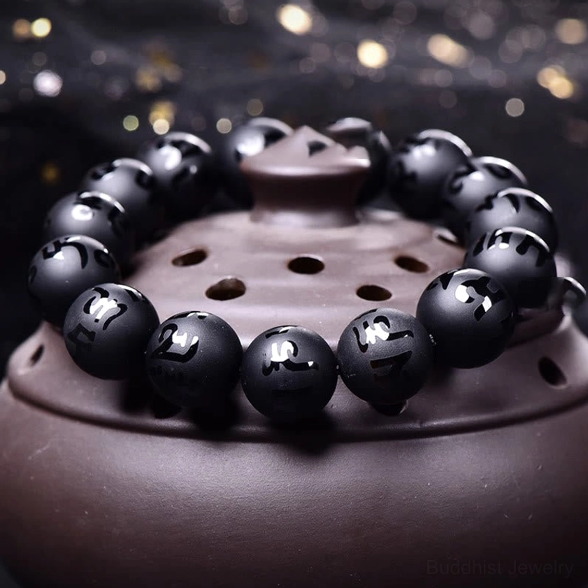 Black onyx beaded bracelet close-up detail on ceramic teapot lid, round matte black beads showcasing carved mantra text with bokeh background