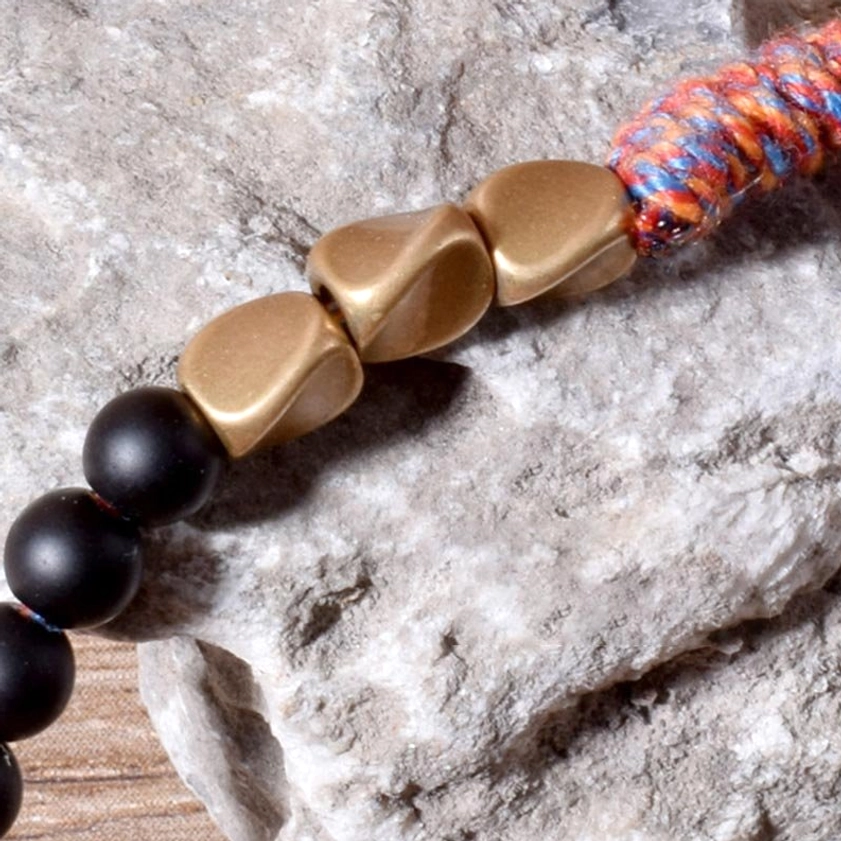 Extreme close-up of black onyx bracelet components showing irregular gold metal beads, matte onyx beads, and intricate tassel weave
