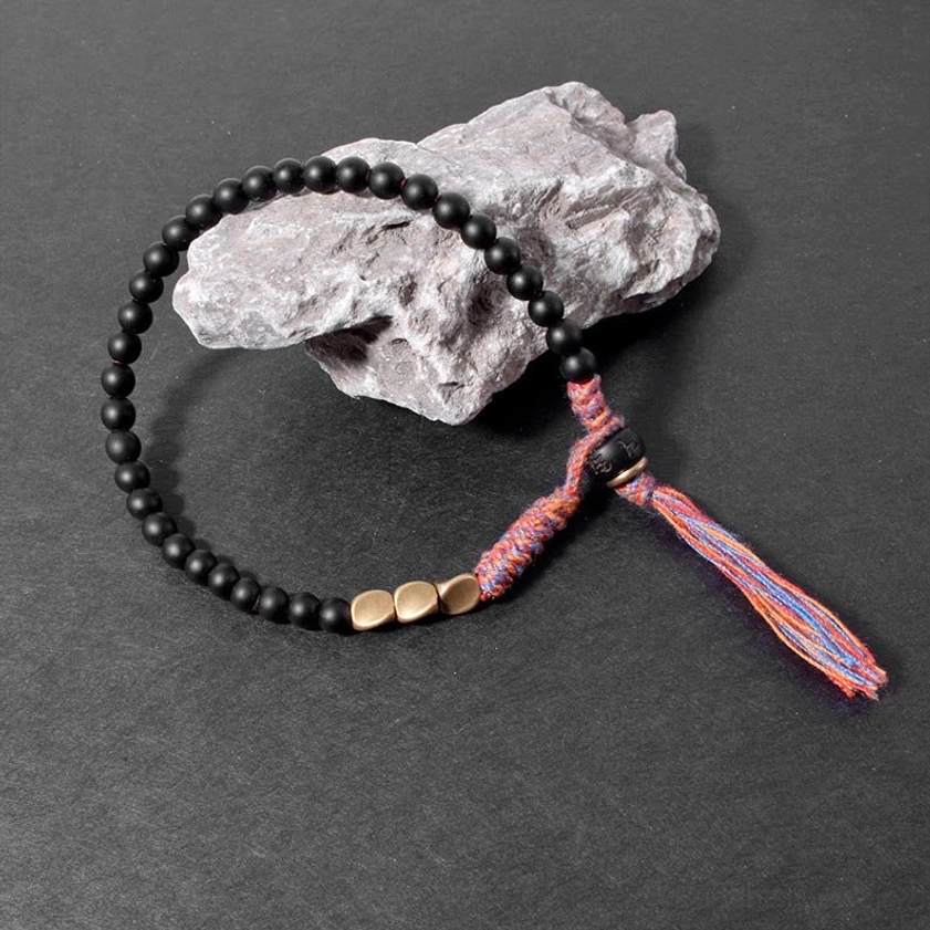 Black onyx protective bracelet side view on stone background, fully extended to show complete woven tassel and bead arrangement