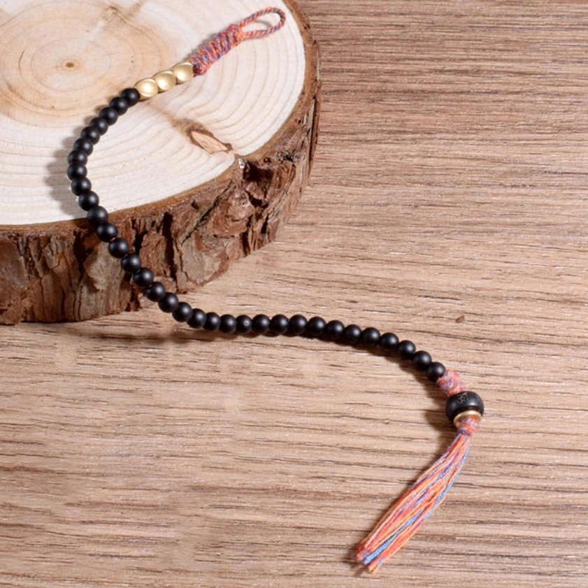 Extended black onyx meditation bracelet on wooden surface, highlighting colorful woven tassel and bead details from low angle
