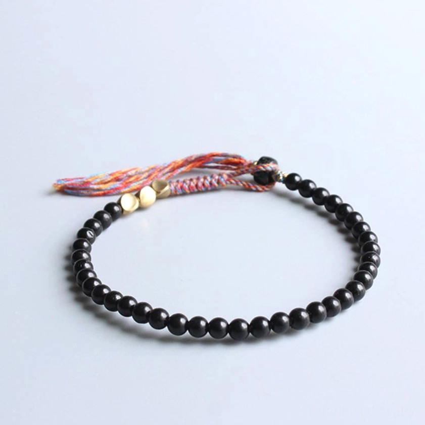 Black onyx mala bracelet side angle view displaying curved beaded structure with brass spacers and mixed-color tassel detail