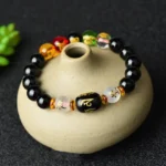 Black onyx Buddhist bracelet with Om Mani Padme Hum mantra bead displayed overhead on ceramic vase, showing glossy gemstone beads and spiritual design