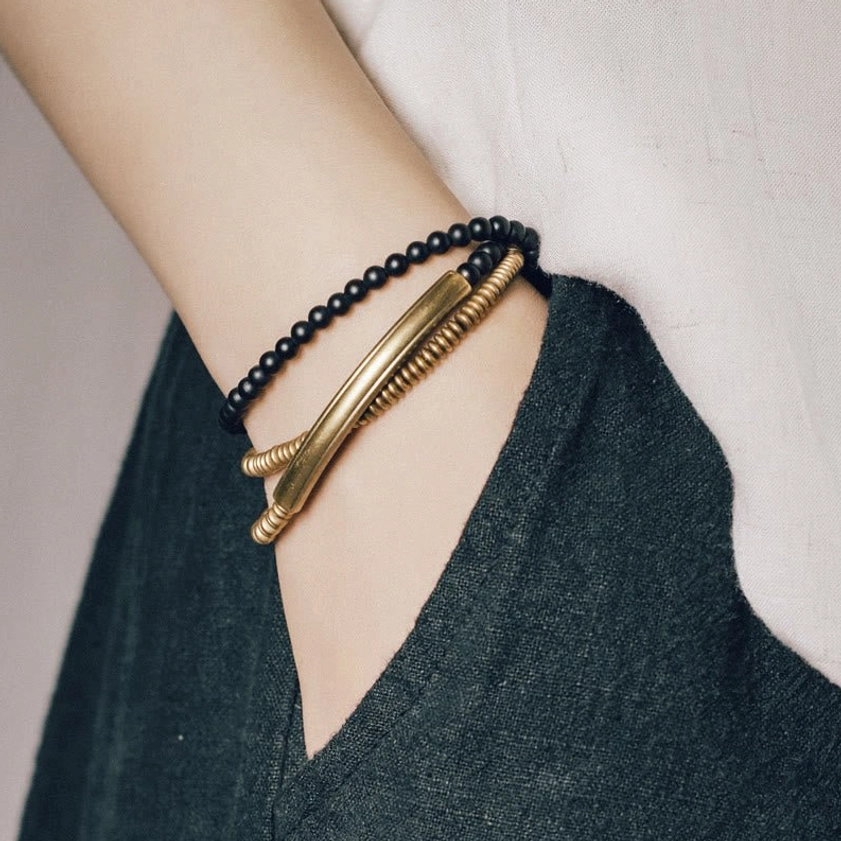 Black agate copper Buddhist bracelet set worn on wrist with linen fabric showing stacked two-piece design with matte black beads and brass metal accents