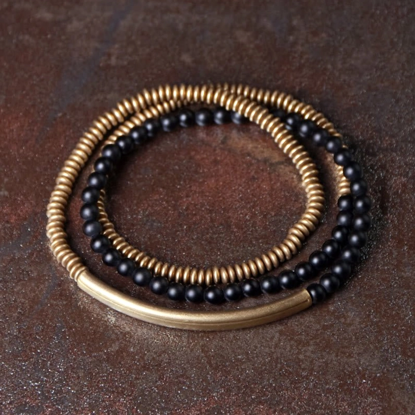 Black onyx copper triple wrap Buddhist bracelet flat lay top-down view on dark rustic desktop with matte black agate beads and brass metal spacers