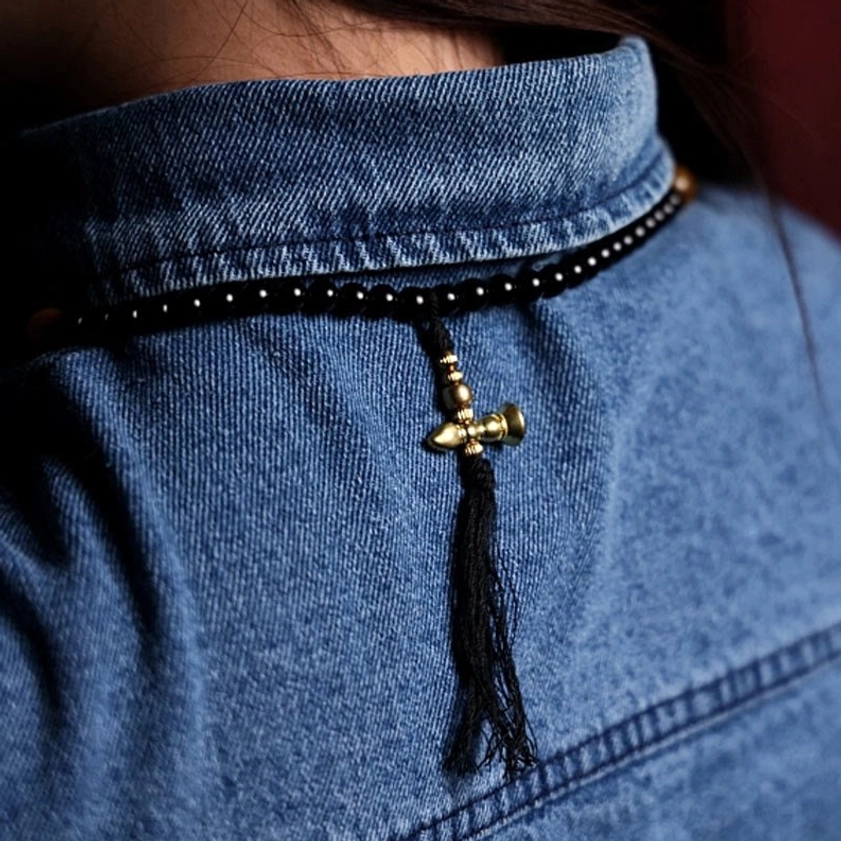 Worn 108 bead mala necklace with black tassel and brass bell pendant on denim shirt