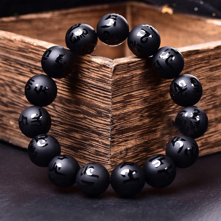Elastic black onyx mantra bracelet displayed in wooden gift box on dark tabletop, showing smooth matte black beads with engraved Sanskrit symbols