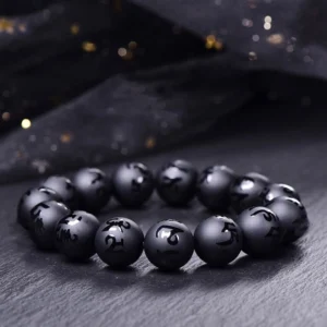 Black onyx Om Mani Padme Hum carved protection bracelet with engraved Sanskrit mantras, flat lay shot showing round matte black beads with mantra text