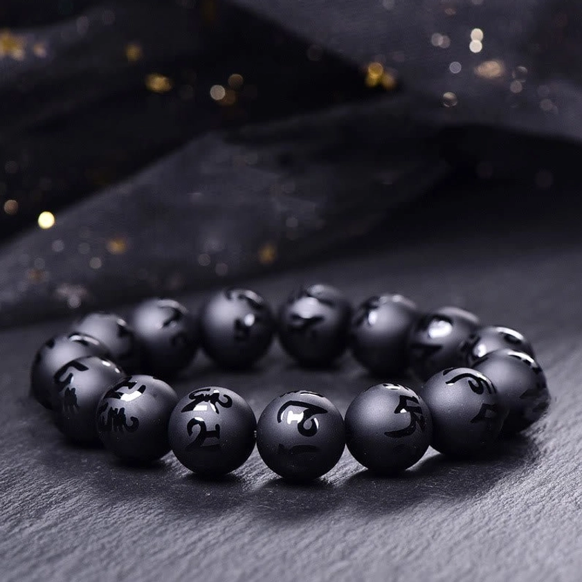 Black onyx Om Mani Padme Hum carved protection bracelet with engraved Sanskrit mantras, flat lay shot showing round matte black beads with mantra text
