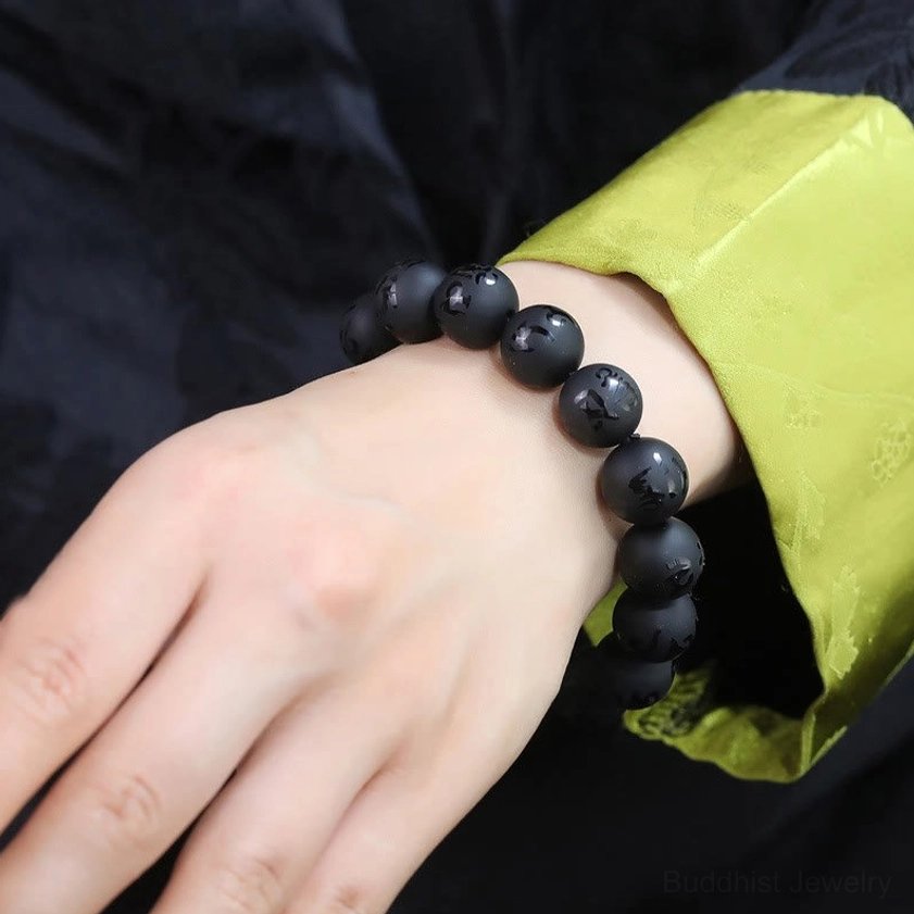 Wearable black onyx mantra bracelet on wrist wearing traditional green sleeve, elastic round matte beads fitting naturally, showing product fit