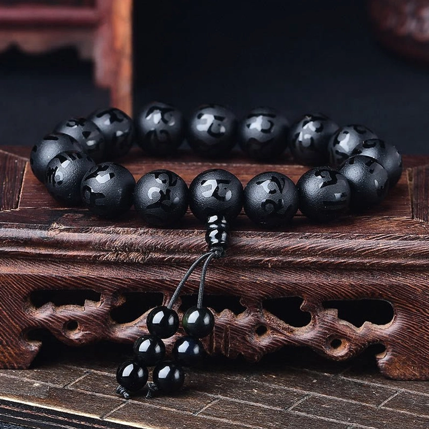 Black Onyx Om Mani Padme Hum bracelet flat lay showcasing protective stone properties and hand-crafted quality with golden tassel embellishment