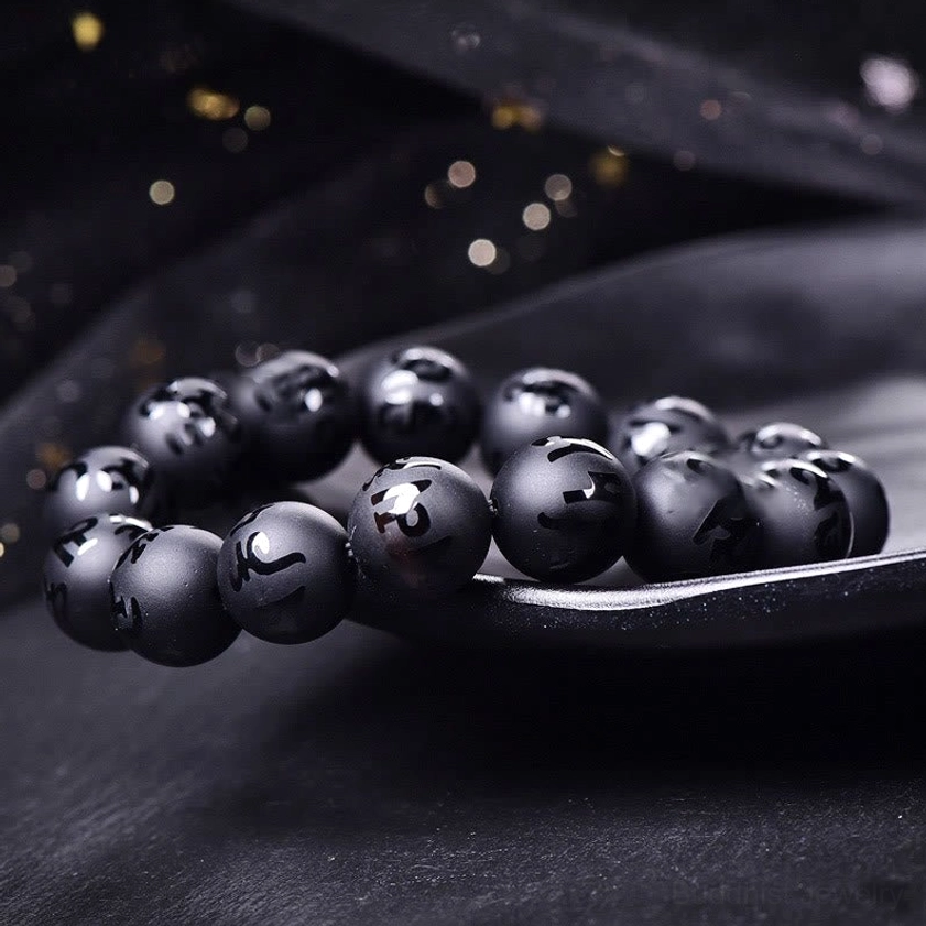 Black onyx engraved mantra bracelet low angle flat lay on ceramic plate, matte round beads with clearly visible Om Mani Padme Hum Sanskrit carvings