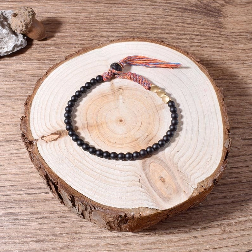 Black onyx prayer bracelet draped over stone on dark gray background, showing matte black beads with gold tone metal accents