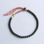 Black onyx tassel bracelet flat lay overhead view showing round matte beads, gold spacers, and colorful woven tassel on neutral background