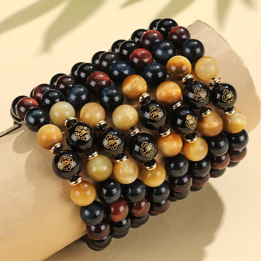 Stacked black onyx tiger eye gemstone bracelets displaying natural stone colors and polished finishes on fabric backdrop