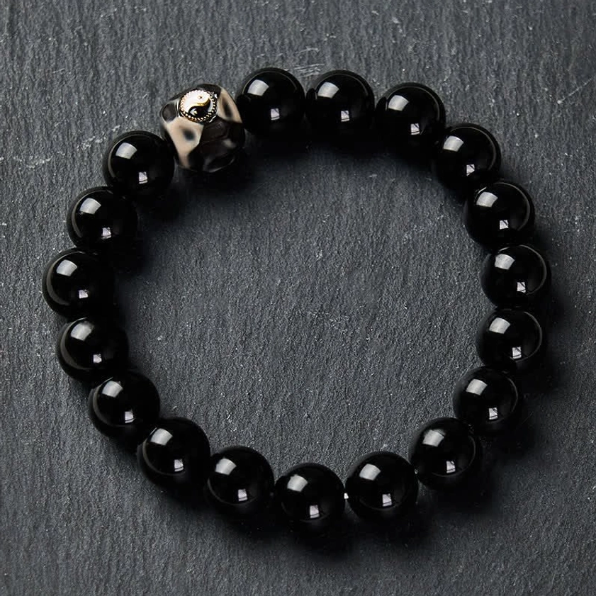 Black Onyx Yin Yang harmony bracelet with polished round beads and central engraved symbol on slate background