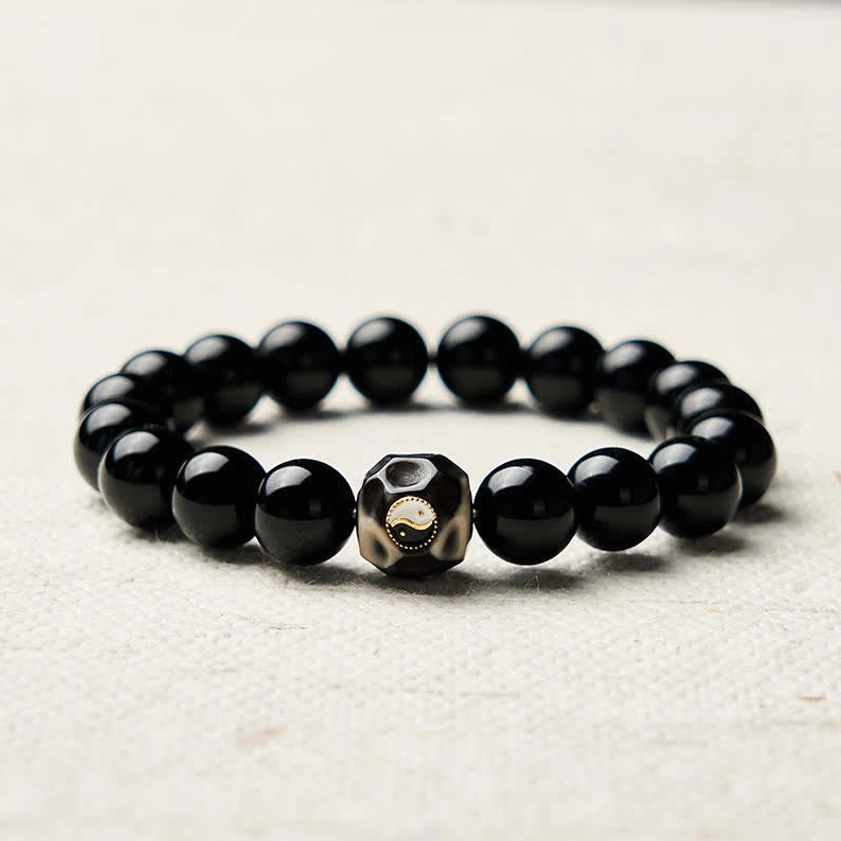 Buddhist Yin Yang protection bracelet with polished black onyx beads and themed accent bead on light beige fabric