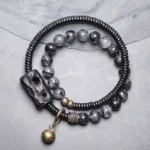 Black rutilated quartz ebony wood copper couple bracelet with carved charm and brass bell pendant on gray surface, top-down view