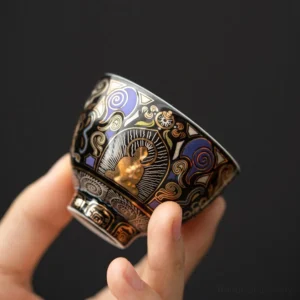 Black Thangka Buddha auspicious clouds ceramic tea cup held in hand, showing intricate gold and purple Buddhist patterns on glossy black ceramic