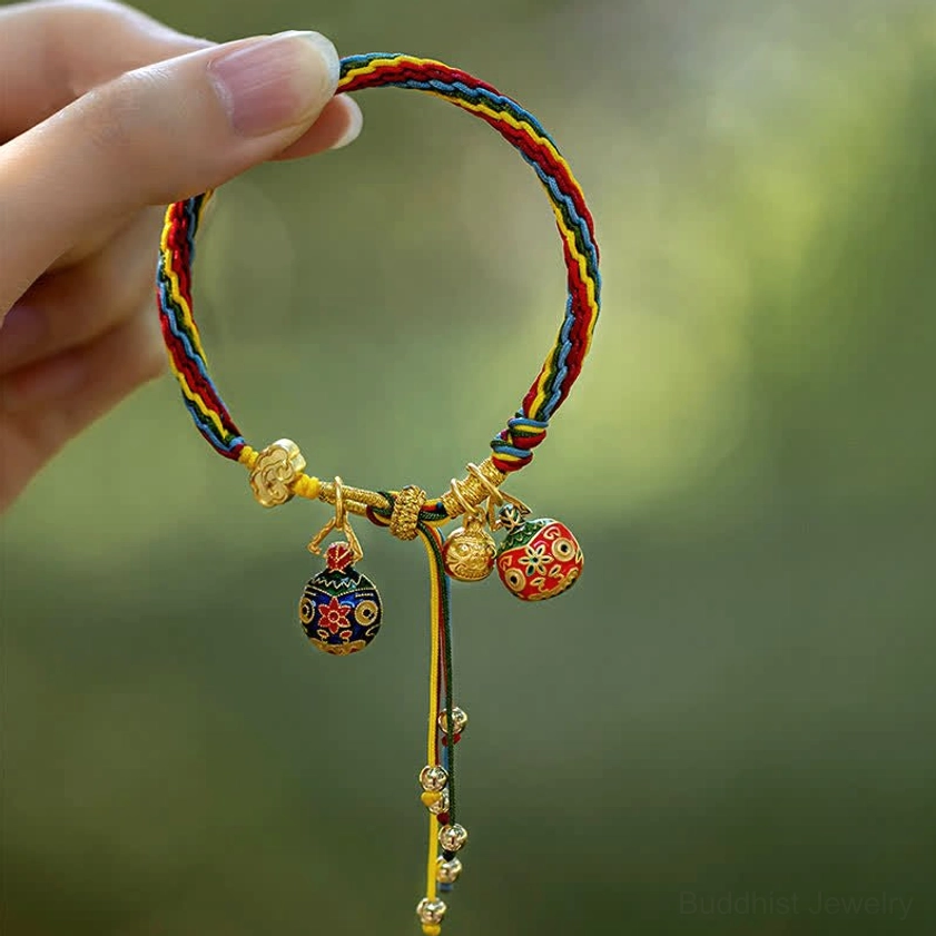 Handcrafted Buddhist bracelet held in hand with multiple enamel charms and tassel bells front view