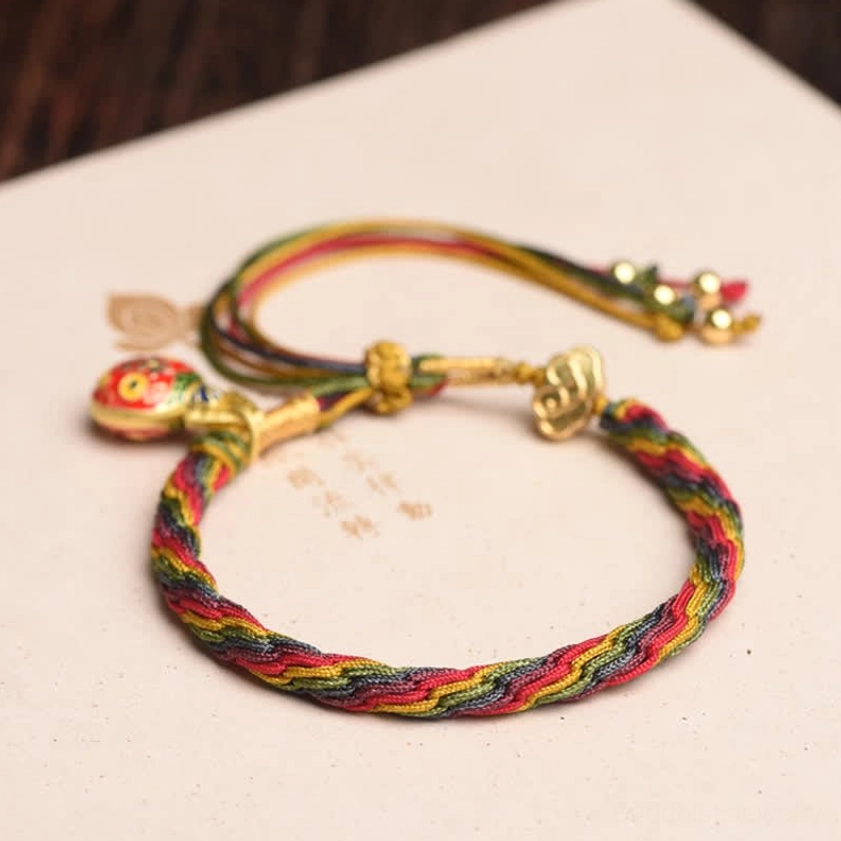 Two handmade Buddhist blessed string bracelets with gold clasps and enamel charms on light background