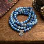 108 blue aventurine mala beads bracelet with silver lotus pendant flat lay on wooden table