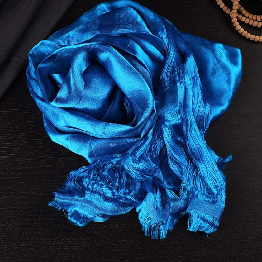 Bright blue five-color Buddhist khata scarf with silk-like satin weave, rolled display on dark wooden table with prayer beads