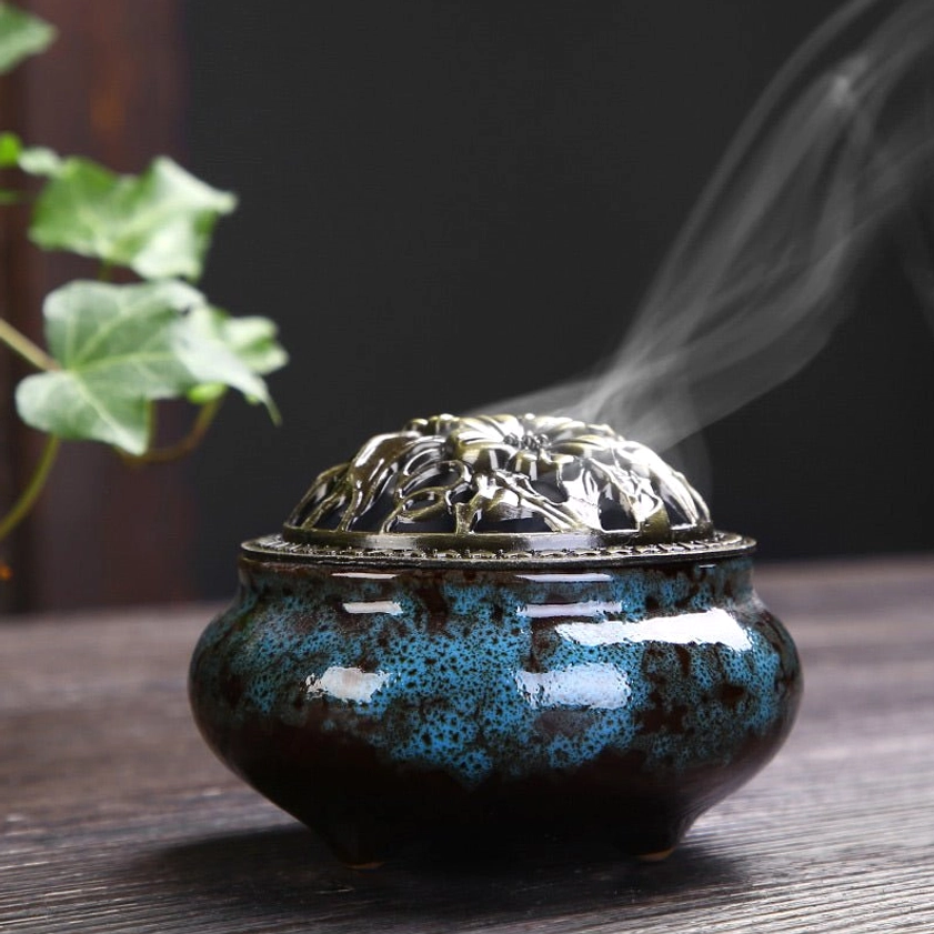 Blue speckled ceramic Buddhist incense burner with ventilated bronze floral lid producing aromatic smoke