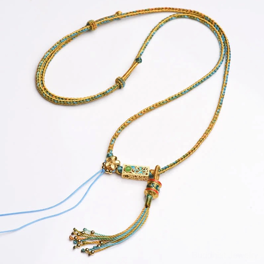 Blue and gold braided copper Buddhist necklace pendant with enamel charm and matching tassel on brown tabletop