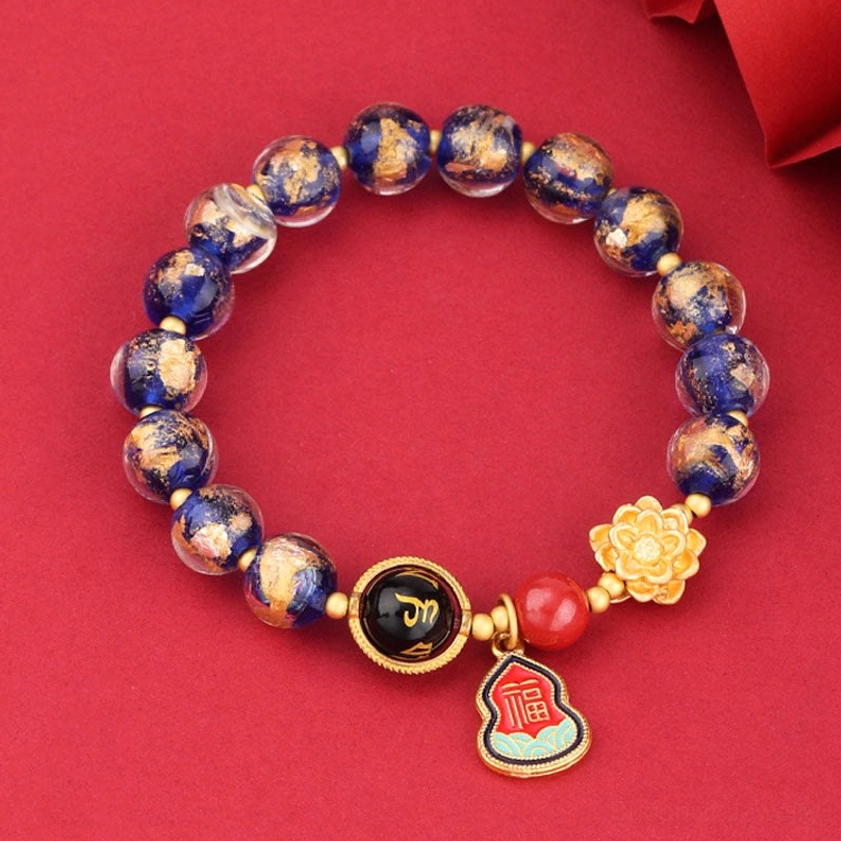 Blue-purple speckled Liuli glass Buddhist bracelet with protective charms and red accent bead on fabric background