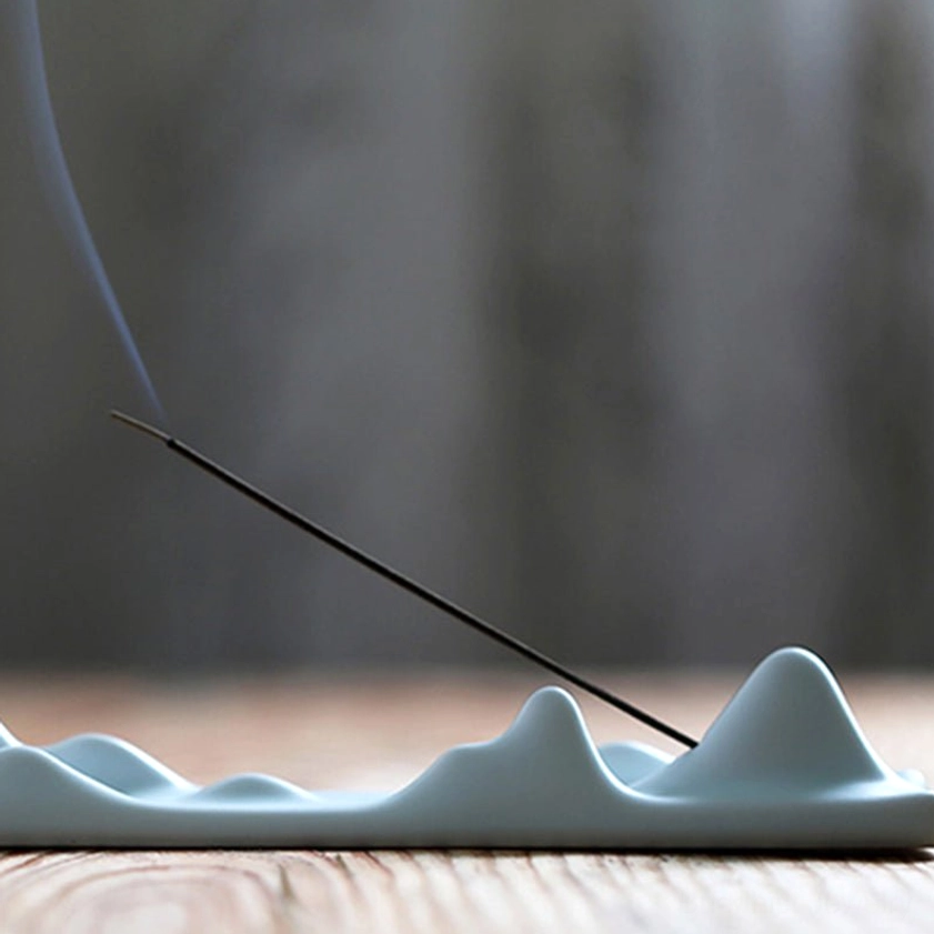 Light blue ceramic mountain peak incense burner on wood background with curling incense smoke