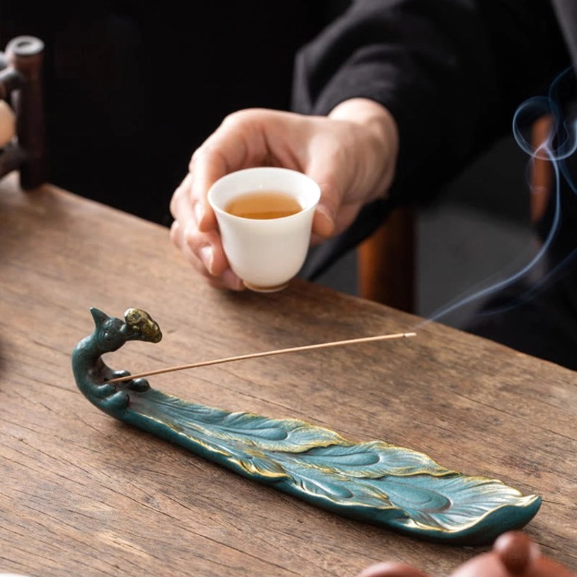 Blue-green peacock incense burner with smoke rising white tea cup meditation setup