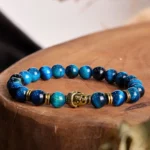 Blue tiger eye Buddha head bracelet with gold charm - overhead flat lay on wooden table