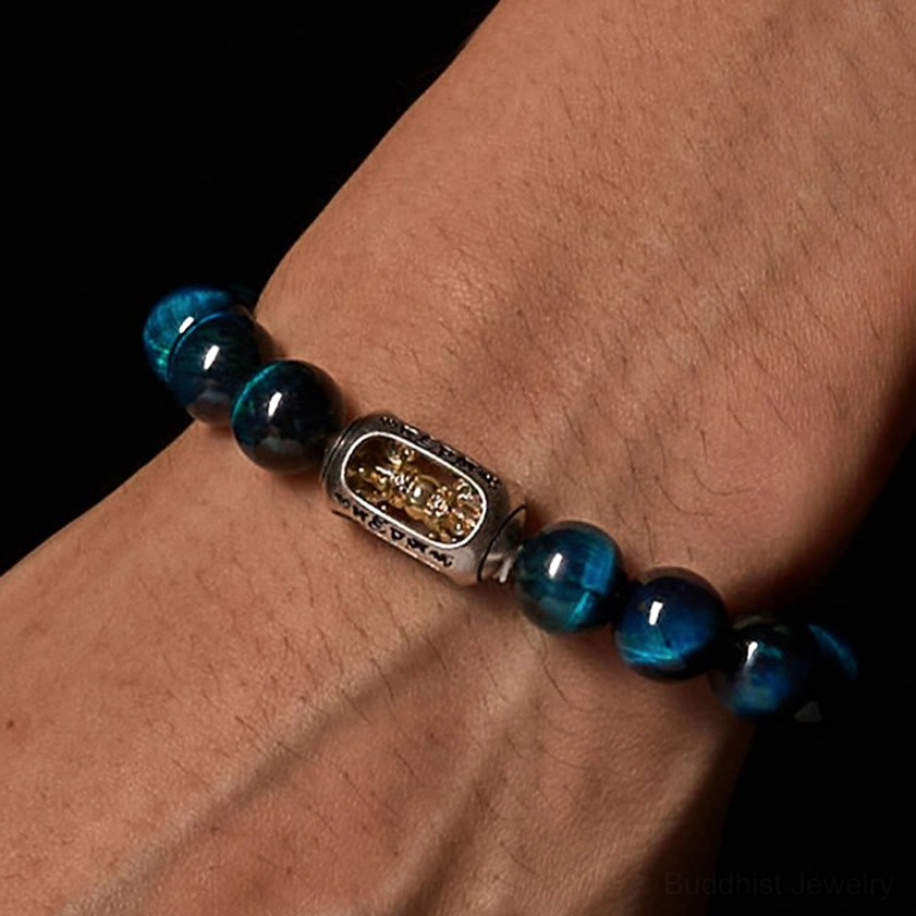 Close-up side view of blue tiger eye bracelet worn on human wrist showing dark blue beads and decorative spiritual mantra charm