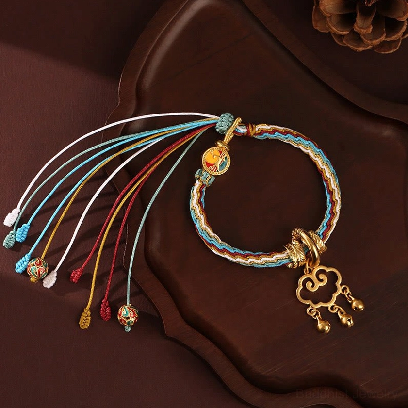 Blue white handmade auspicious cloud lock bracelet with multicolor braided ropes, gold cloud lock pendant and assorted tassel charms on dark wooden tray