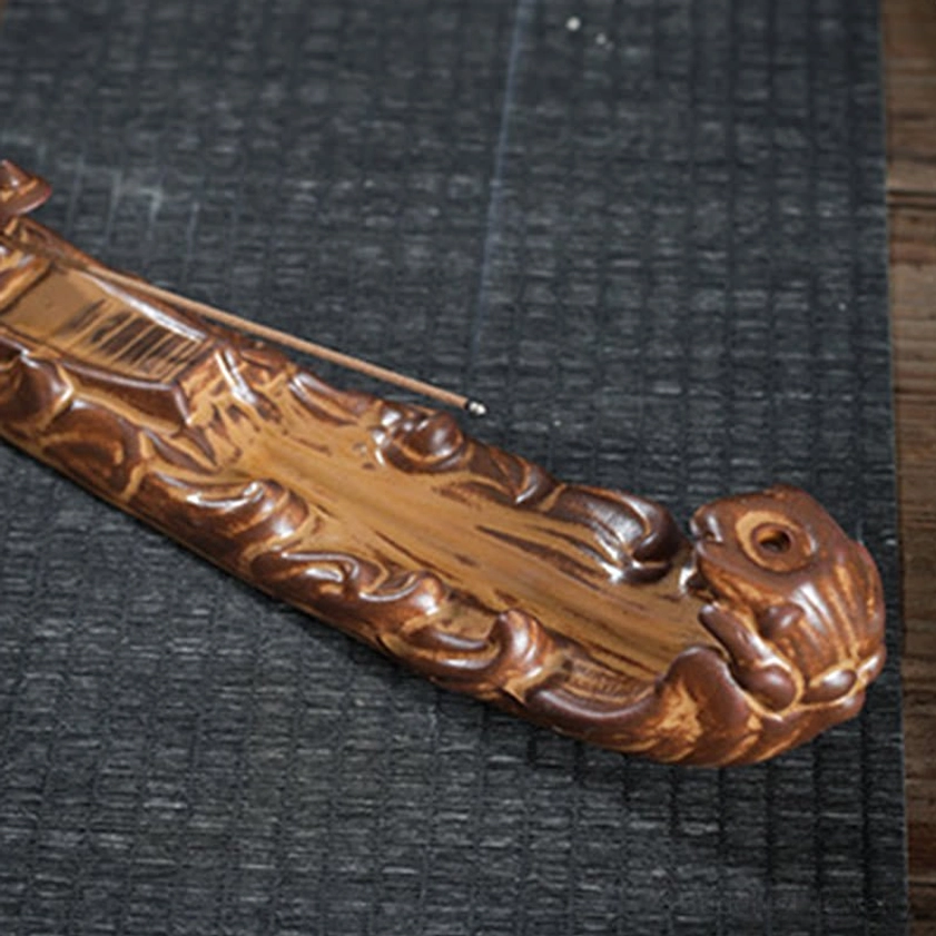 Overhead close-up of handcrafted boat incense burner with mythical beast head and wavy textured body on dark mat