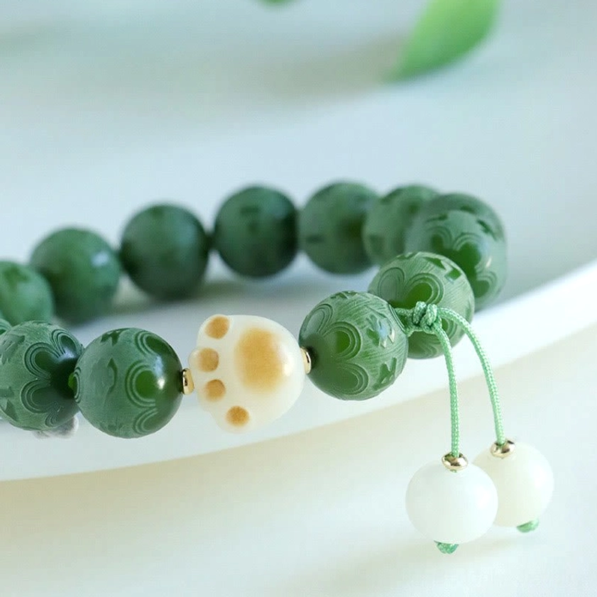Close-up detail of carved Bodhi Seed beads showing Om Mani Padme Hum mantra inscriptions and paw-print jade accent charm