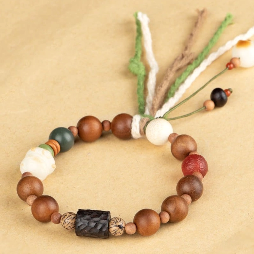 Flat lay of wooden beaded tassel bracelet featuring green accent beads, red agate stone, and multi-strand cotton decoration