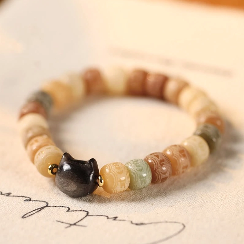 Bodhi seed Om Mani Padme Hum bracelet with carved beads and silver sheen obsidian cat head charm on desk backdrop