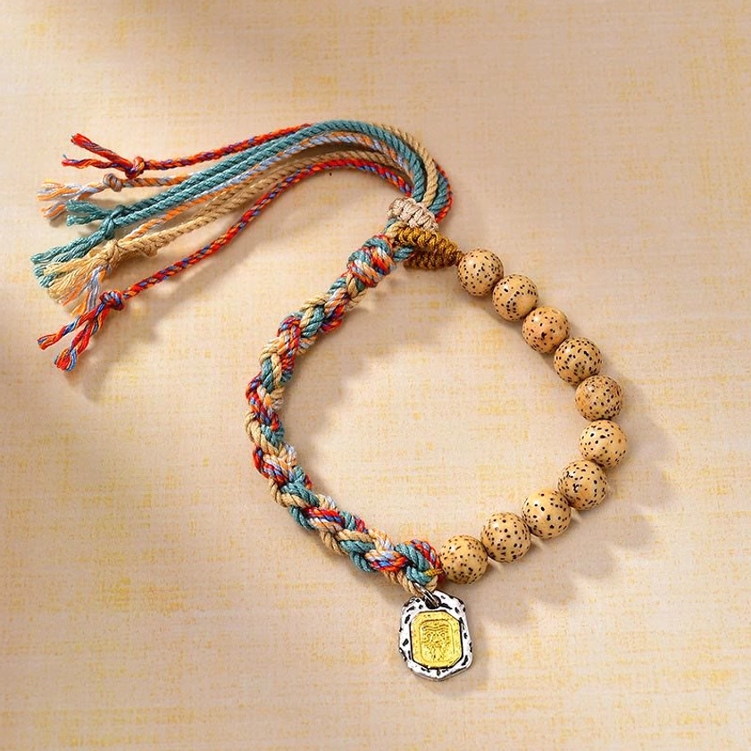 Top-down view of adjustable bodhi seed wealth bracelet with multicolor woven rope, metal charm, and tassel design
