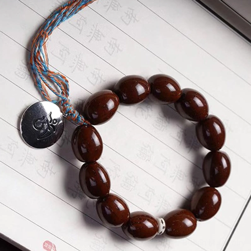 Bodhi charm bracelet rested on palm showing reddish-brown beads and silver medallion with tassel