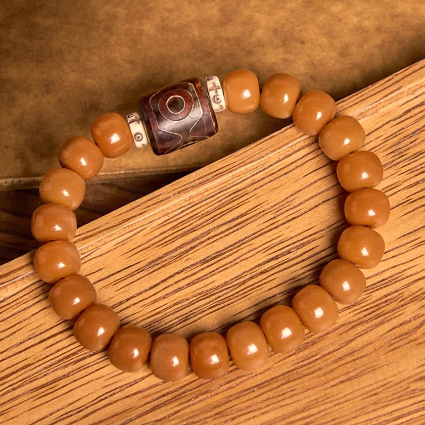 Bodhi seed Dzi bead bracelet angled view showing warm orange-brown barrel beads with dark red protective Dzi bead and metal spacers on wooden board