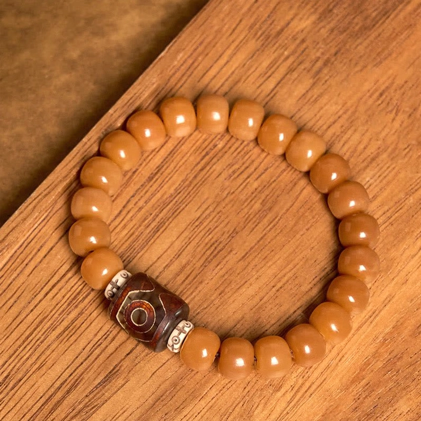 Bodhi seed and hand-painted Dzi bead bracelet flat lay with light tan barrel beads, three-eyed Dzi bead, and silver metal spacers on wooden surface