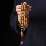 Bodhi seed Buddhist bracelet with three-eye Dzi bead and carved Buddha hand charm held in palm close-up