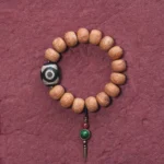 Bodhi seed and hand-painted dzi bead Buddhist mala bracelet with green copper pendant on dark red background