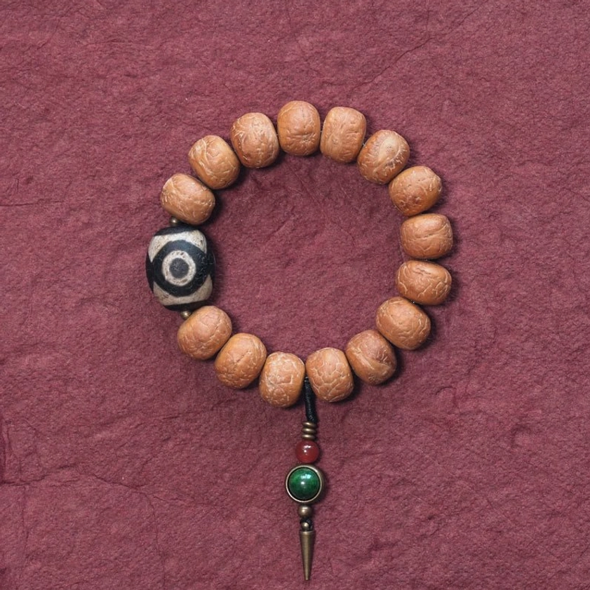 Bodhi seed and hand-painted dzi bead Buddhist mala bracelet with green copper pendant on dark red background