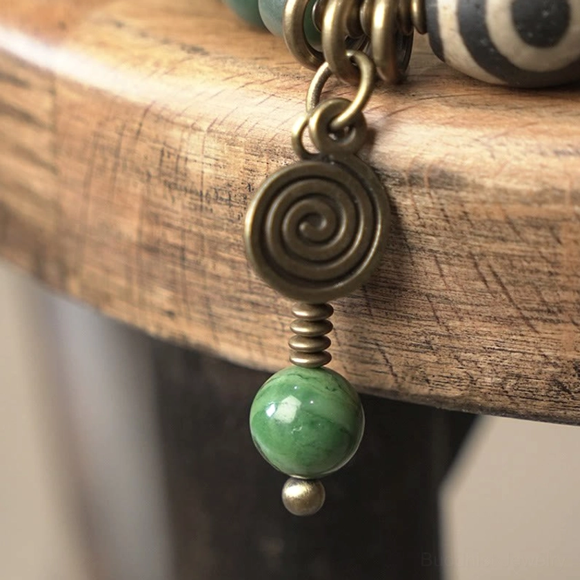 Macro view of bracelet charm pendant with bronze spiral element and matte green bodhi bead drop