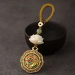 Bodhi seed hetian jade lotus rotatable keychain with yellow braided rope and white lotus enamel charm, displayed with ceramic bowl