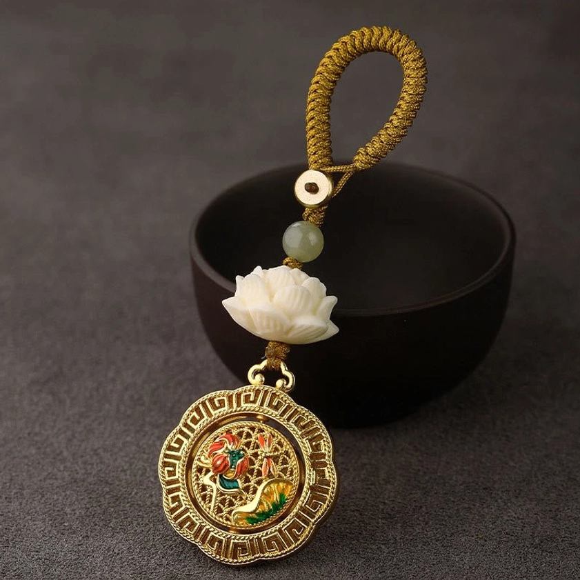 Bodhi seed hetian jade lotus rotatable keychain with yellow braided rope and white lotus enamel charm, displayed with ceramic bowl